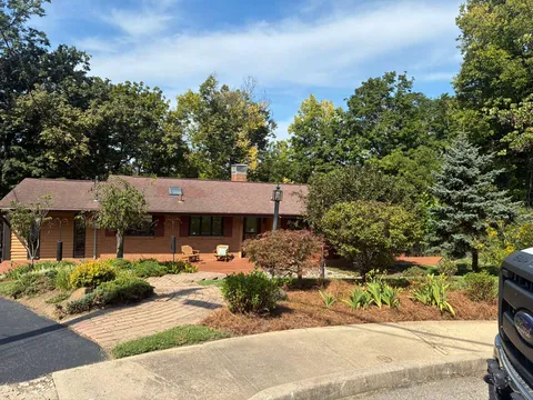 Wide view of a landscaped residential yard with trees, shrubs, and a paver walkway